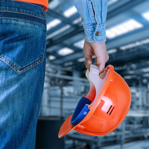 Worker standing in jeans and holding a bright orange construction helmet at their side.