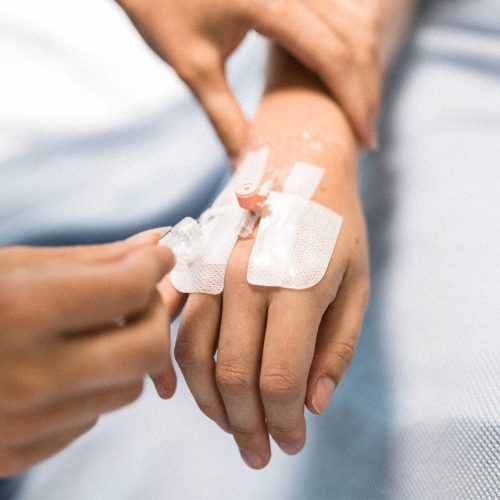 Caregiver adjusting the flow of liquid through an IV inserted in the back of a hand.
