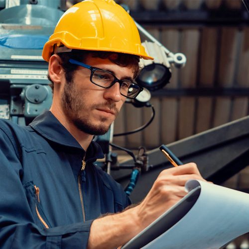 Plant worker with glasses, yellow safety helmet, and clip board taking notes.